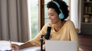woman of color wearing headphones at desk with laptop and microphone recording a podcast